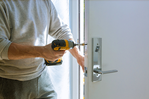 homme qui repare la serrure d'une porte à l'aide d'une dévisseuse